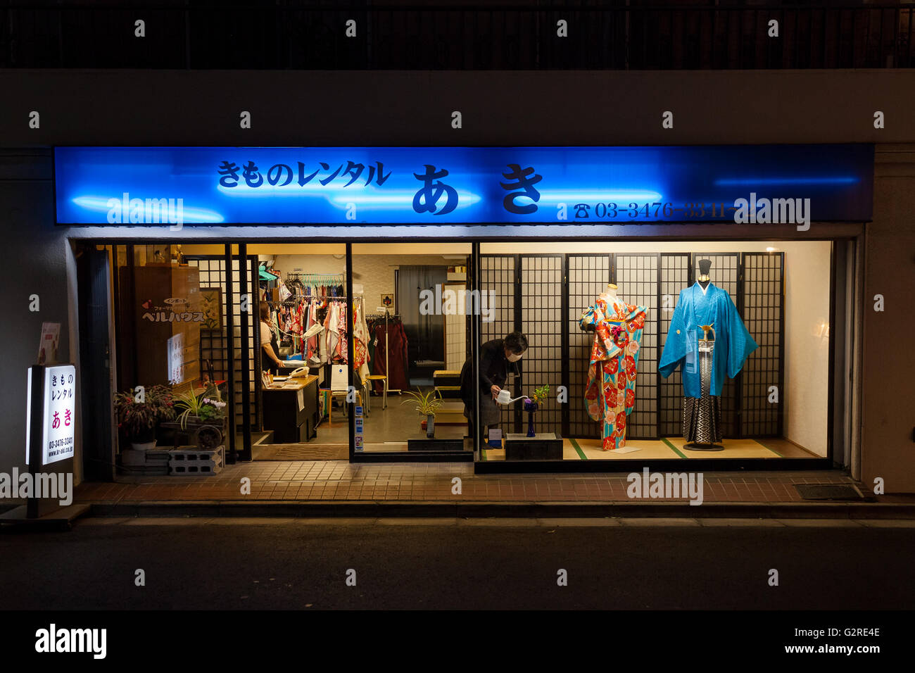 Eine Frau wässert eine Pflanze im Schaufenster eines Kimono-Shops in Dogenzaka, Shibuya, Tokio, Japan. Stockfoto