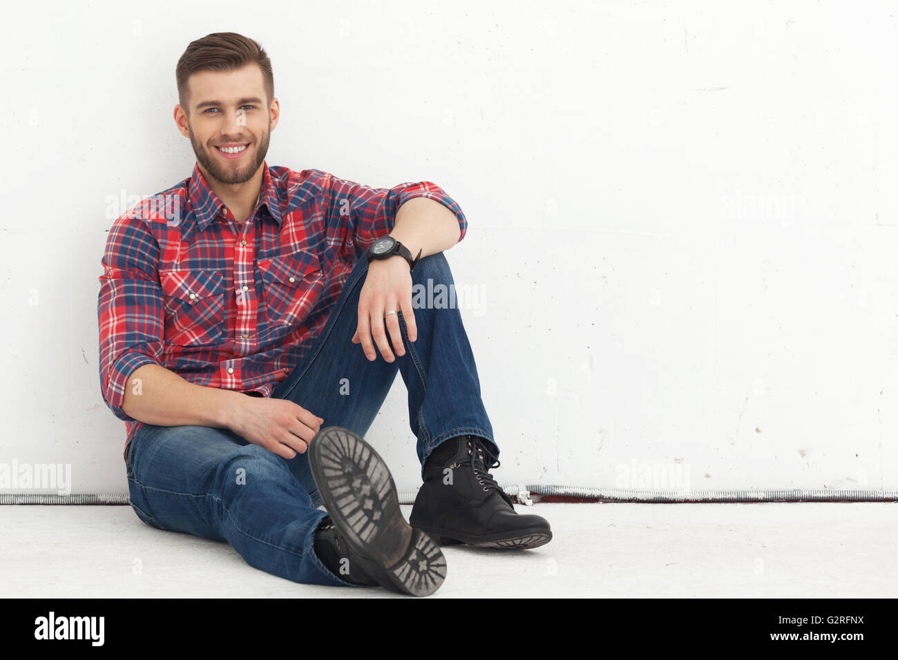 Porträt von glücklichen hübscher junger Mann in Freizeitkleidung gegen weiße Wand sitzen. Stockfoto