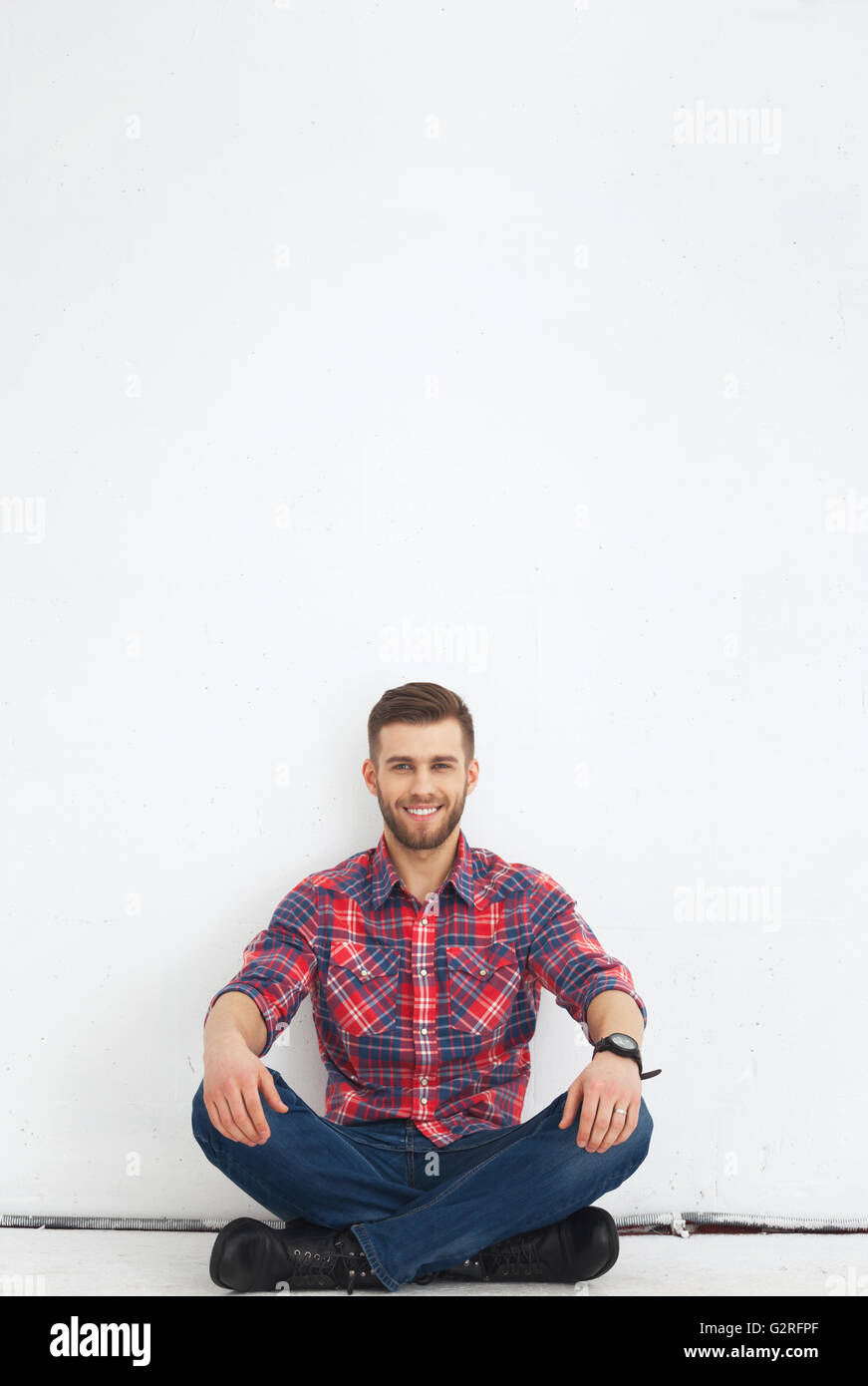 Porträt von glücklichen hübscher junger Mann in Freizeitkleidung gegen weiße Wand sitzen. Stockfoto