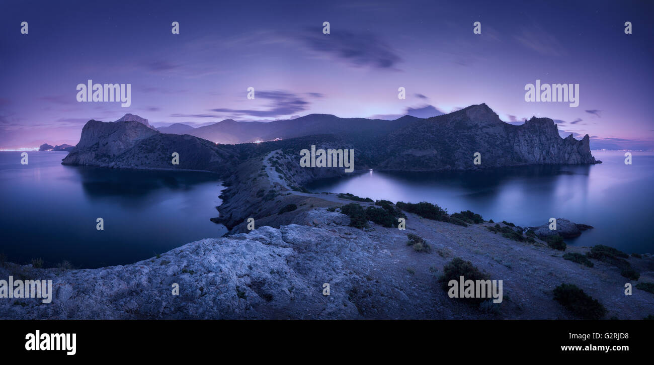 Nacht-Landschaft mit Bergen, Meer, Sternenhimmel und Lichter der Stadt. Herrliche Aussicht mit Steinen in der Abenddämmerung auf der Krim Stockfoto