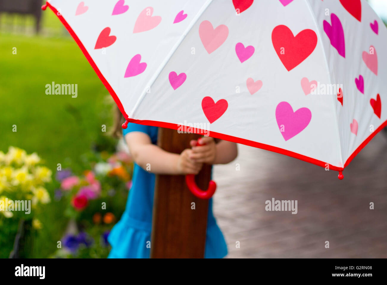 Kindergarten-Alter Mädchen versteckt ihr Gesicht hinter einem hellen Schirm mit Blumen und Gräser im Hintergrund. Stockfoto