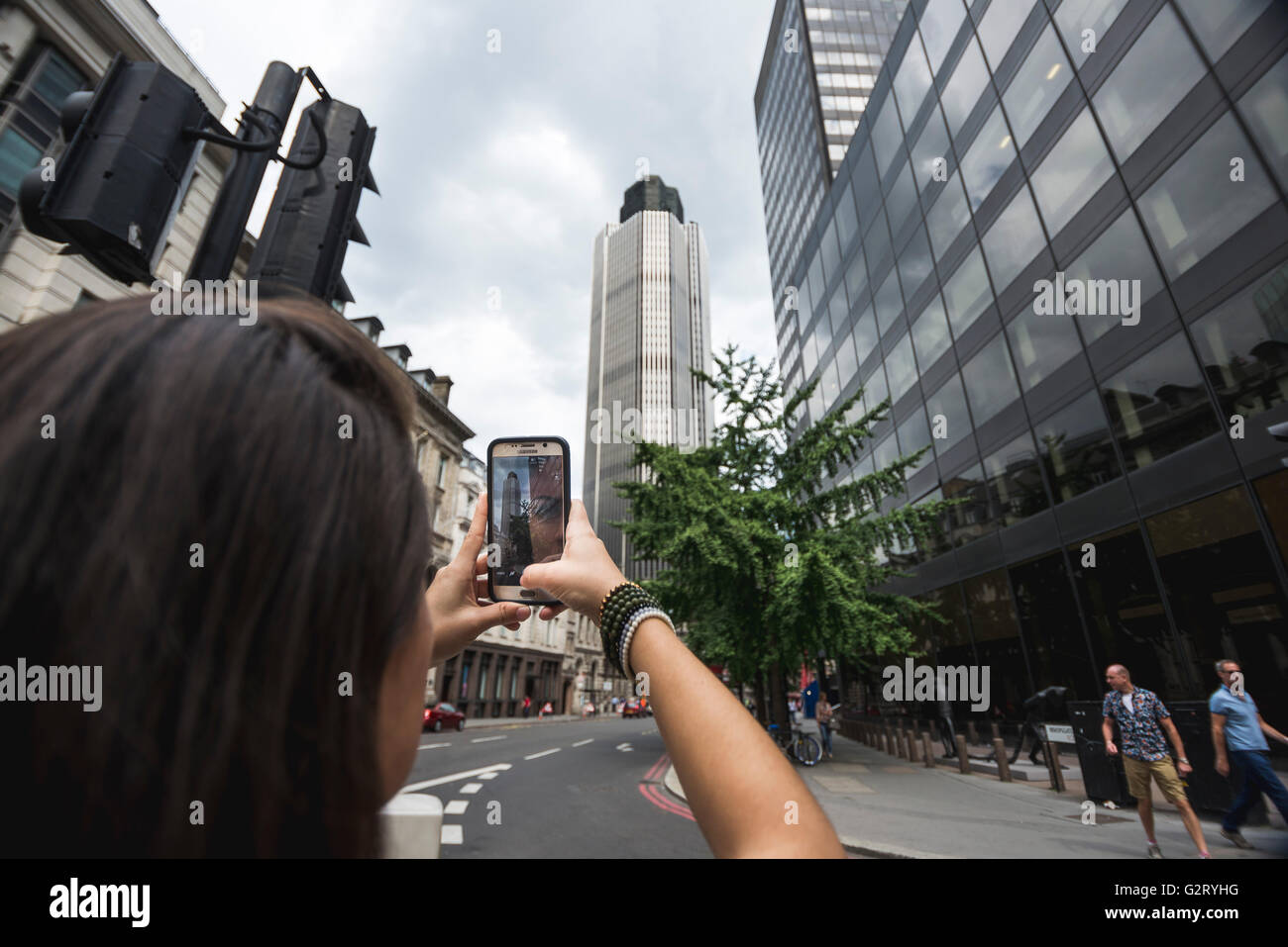 Eine junge Frau, die eine Aufnahme mit ihrem Smartphone auf dem Bürgersteig ein London Street, England. Stockfoto