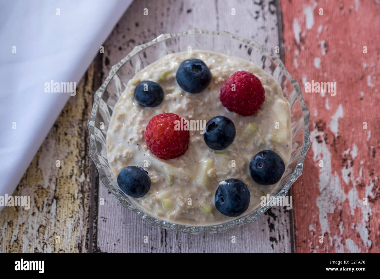 Obenliegende Bild von hausgemachten Birchermüesli mit Sommerfrüchten in Glasschale mit Serviette auf hölzernen Hintergrund Stockfoto