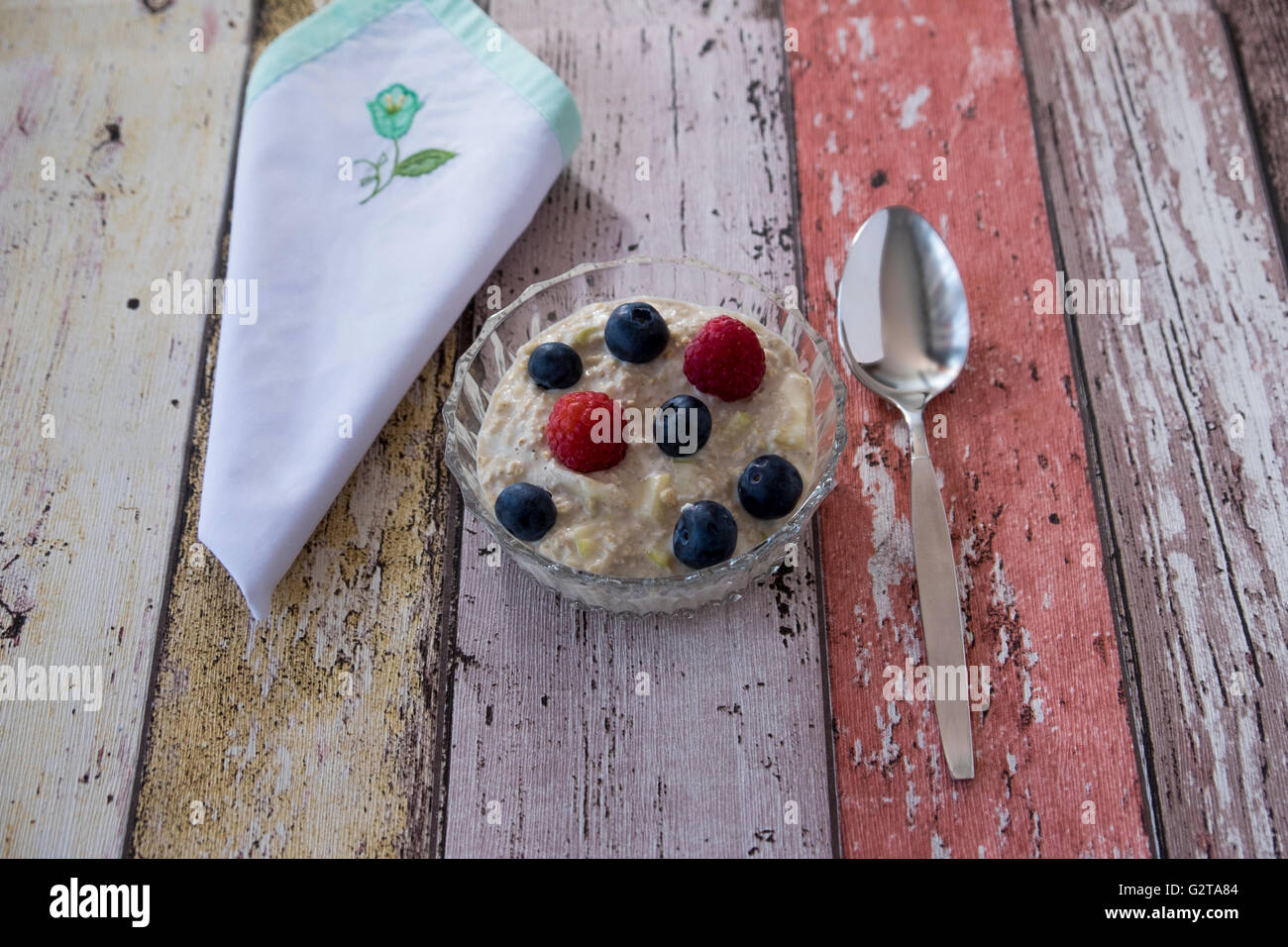 Flach Bild von hausgemachtem Bircher Müsli in Glasschale mit Serviette und Löffel auf hölzernen Hintergrund Stockfoto