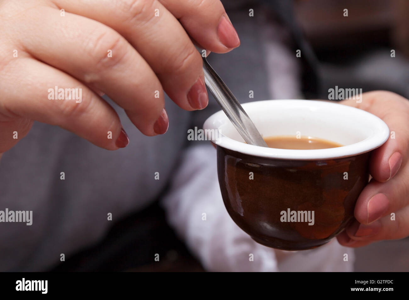 Frau in einer Kaffee-Bar ihre morgendliche Tasse Kaffee und Milch mit einem kleinen Löffel umrühren. Stockfoto