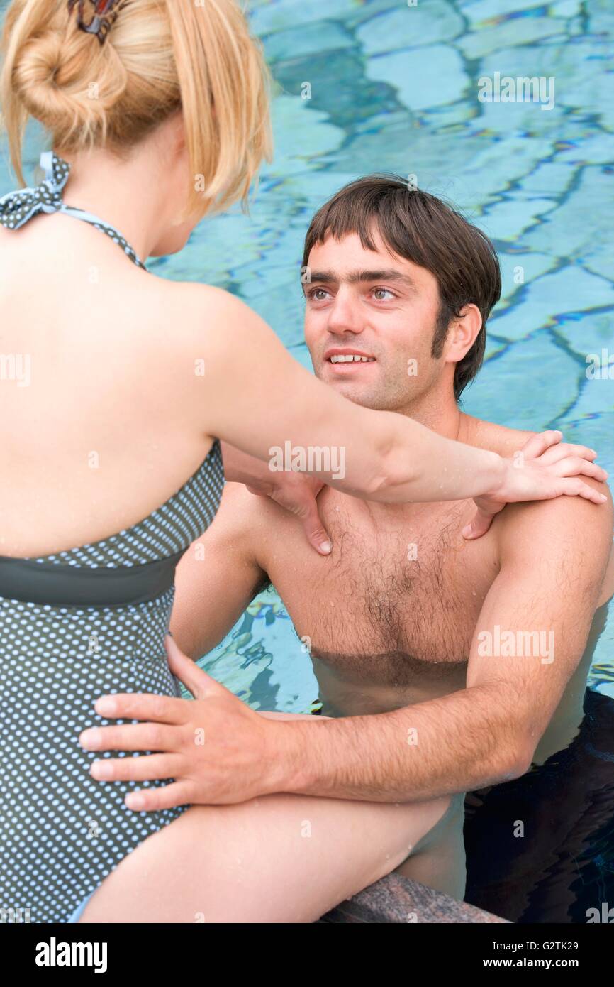 Frau sitzt am Rand des Pools, Mann vor ihr im Wasser Stockfoto
