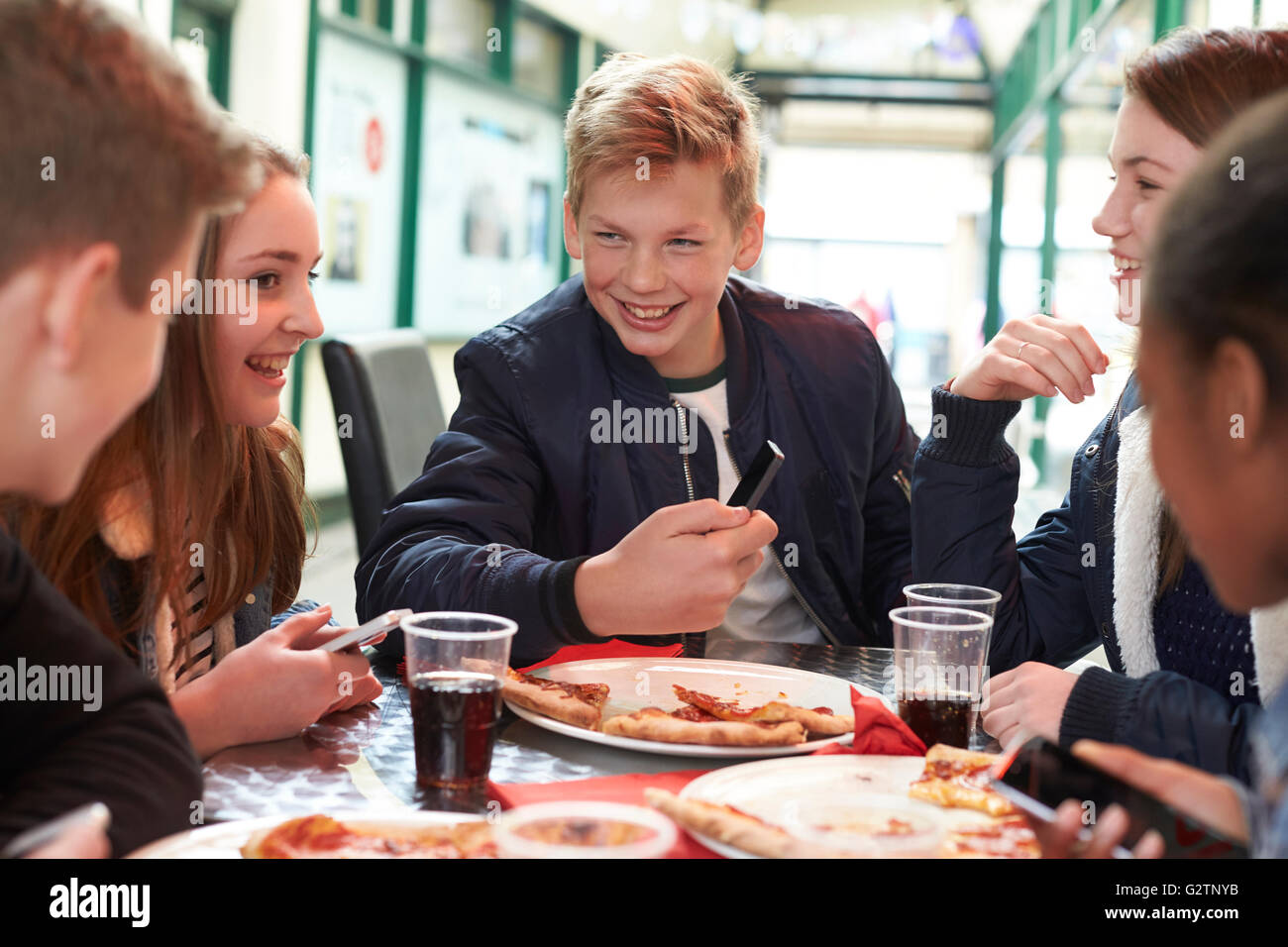 Jugendliche essen Pizza Cafe und Blick auf Handy Stockfoto