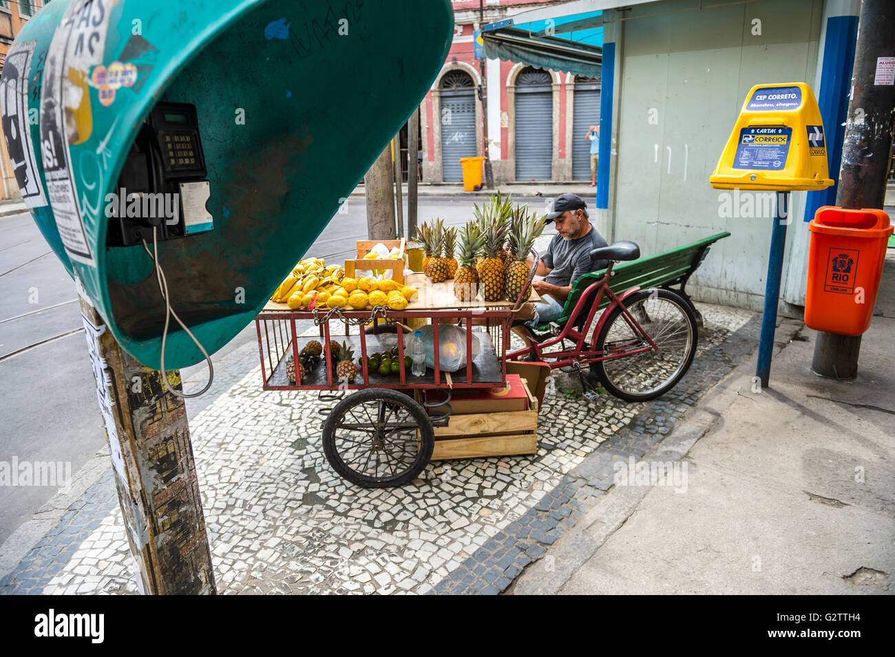 RIO DE JANEIRO - 24. März 2016: Brasilianische Obstverkäufer sitzt zwischen einem traditionellen Telefonzelle und Briefkasten in Santa Teresa. Stockfoto