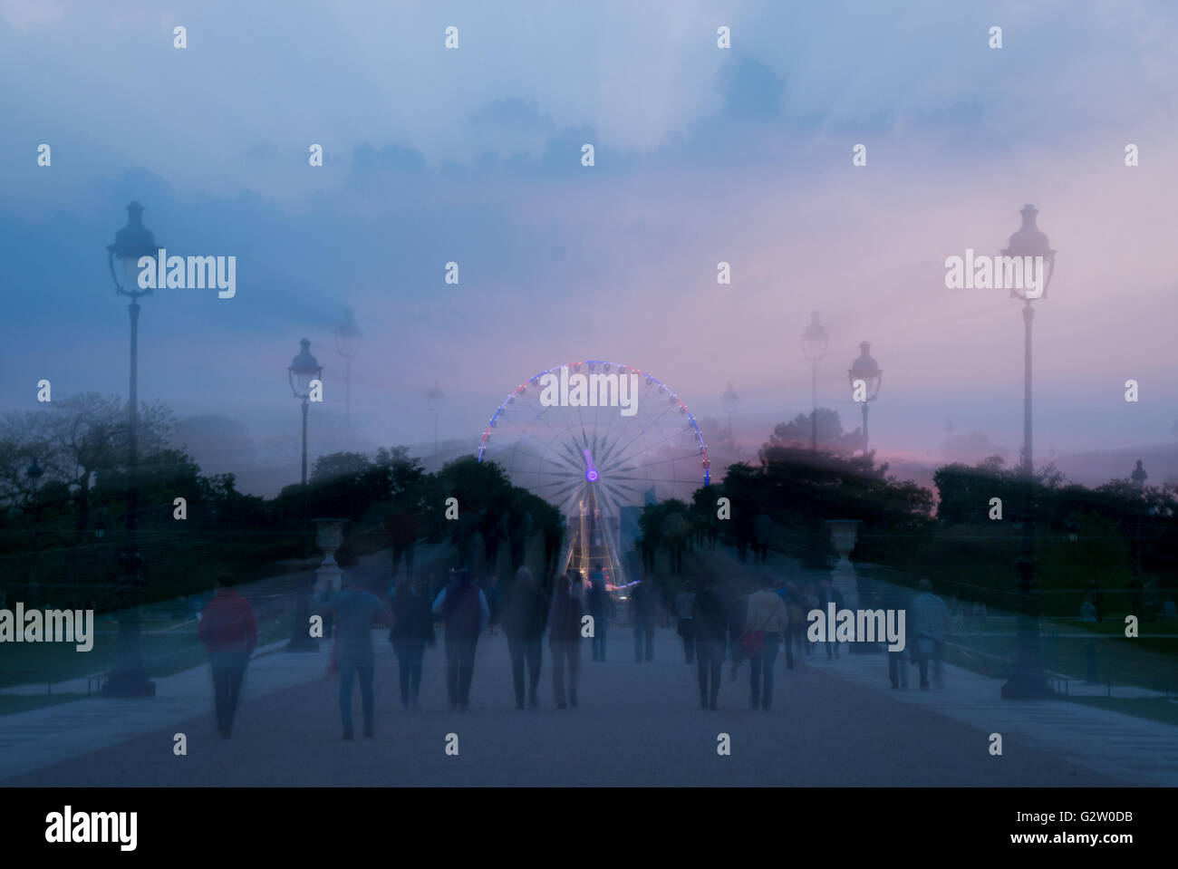 Ein "Zoom Burst" Effekt Bild von Menschen zu Fuß durch die Tuilerien in Paris in der Dämmerung mit einem Riesenrad im Hintergrund. Stockfoto