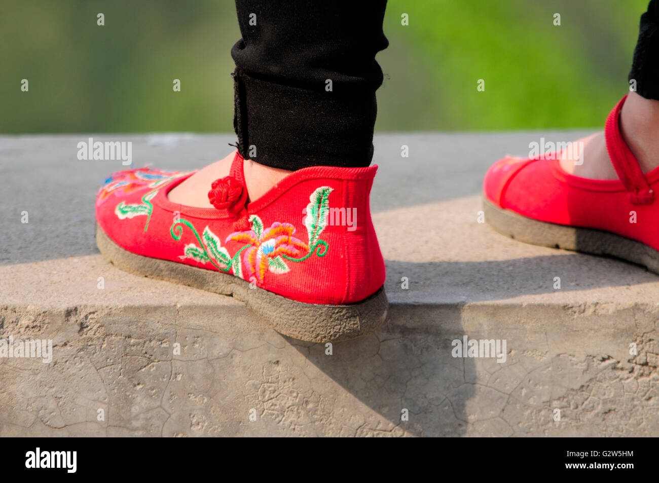 Eine Frau trägt traditionelle Hand machte chinesische Schuhe und stehen auf einer Betonmauer in Jingshan Park Peking China. Stockfoto