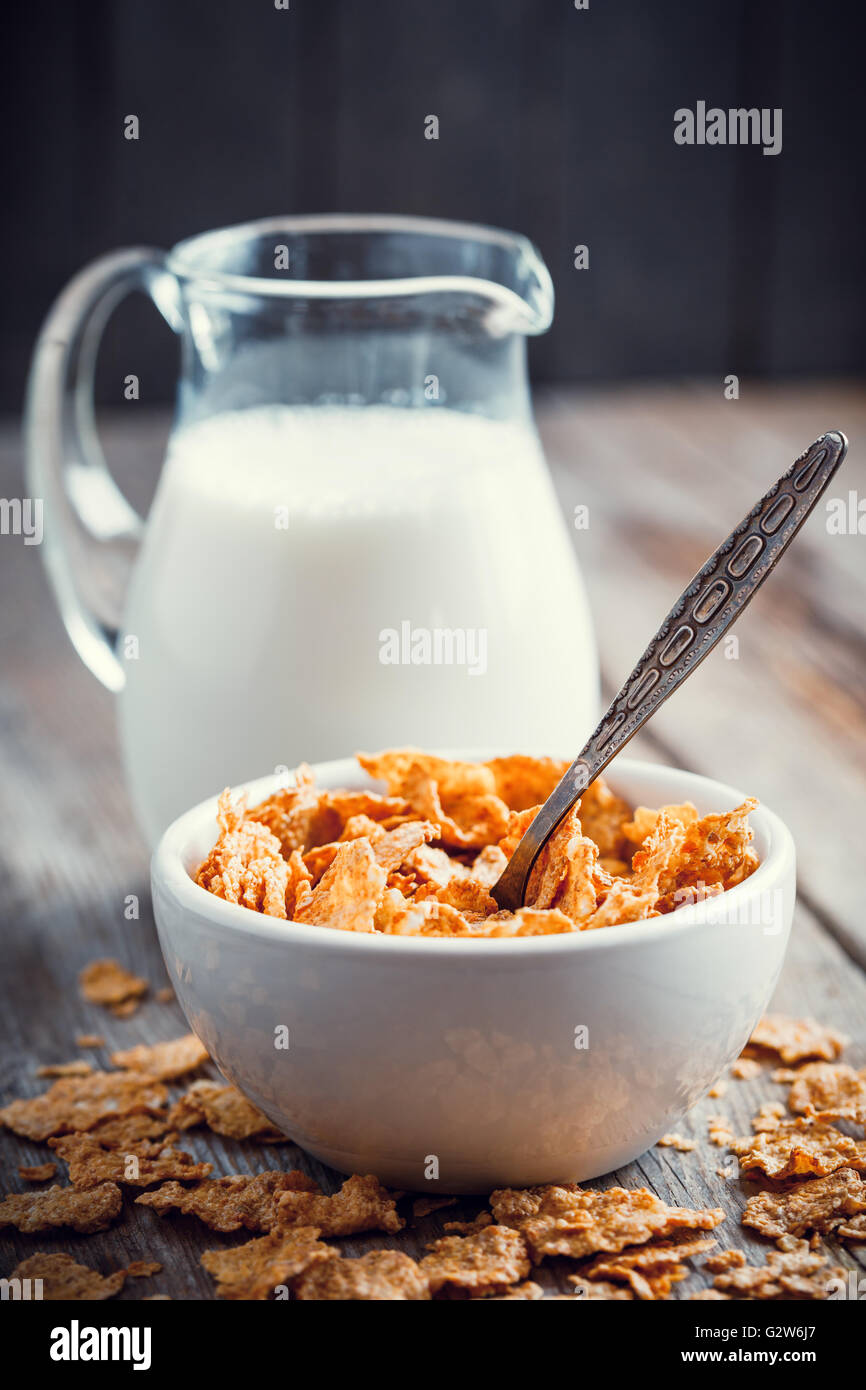 Frühstück Getreideflocken Weizen in Schüssel und Milch Krug auf Holztisch Stockfoto