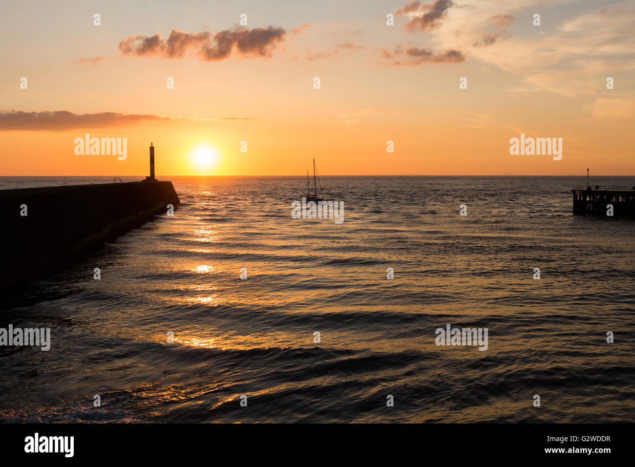 Die untergehende Sonne über dem Horizont an der Westküste von Wales als Yacht kehrt zurück zum Hafen Stockfoto