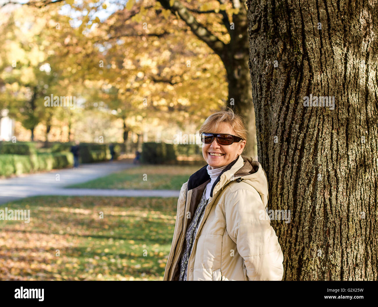 Reife, lächelnde Frau im Herbst Park am Baum, horizontale Stockfoto