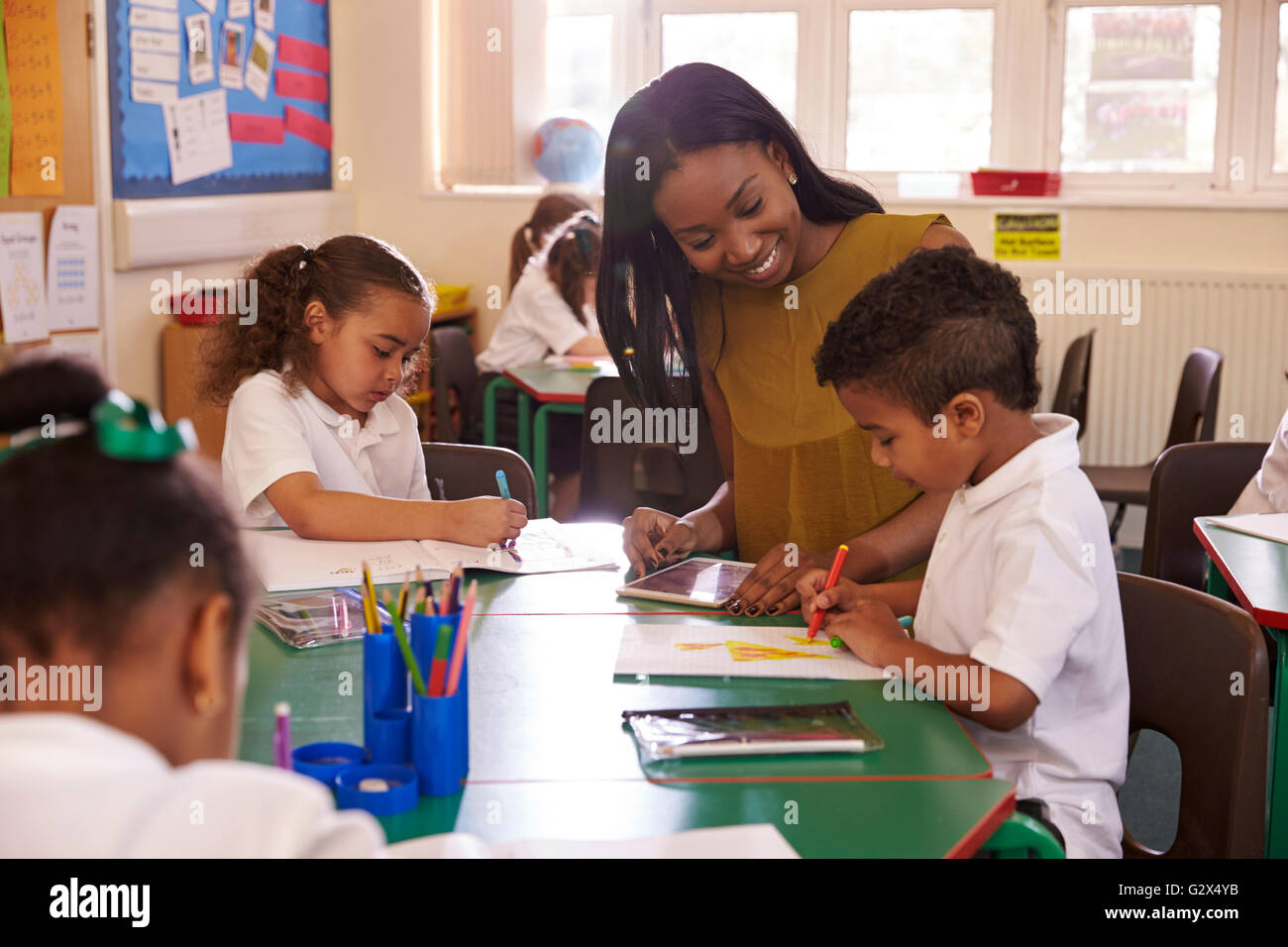 Weibliche Grundschullehrerin helfen Schülern am Schreibtisch Stockfoto