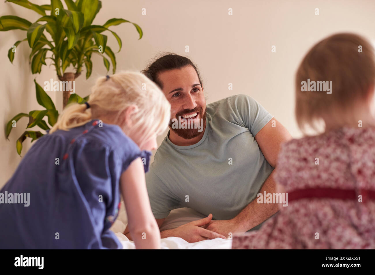 Töchter auf Bett sitzend mit Vater Stockfoto