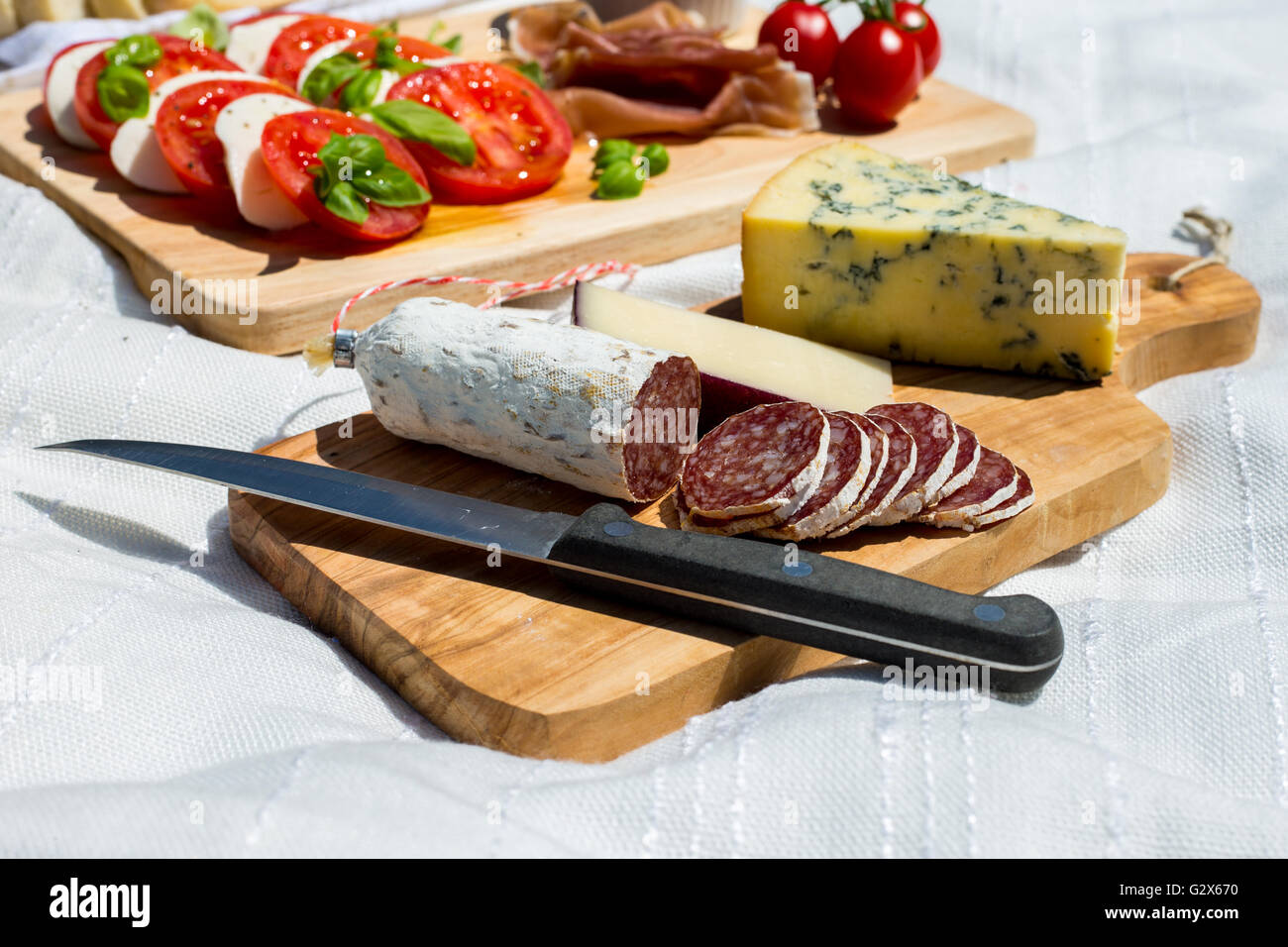 Nahaufnahme der geschnittene Salami in ein Picknick mit Tomatensalat mit Mozzarella, Parmaschinken, Erdbeeren, Oliven und Espressokanne in einem Park. Stockfoto