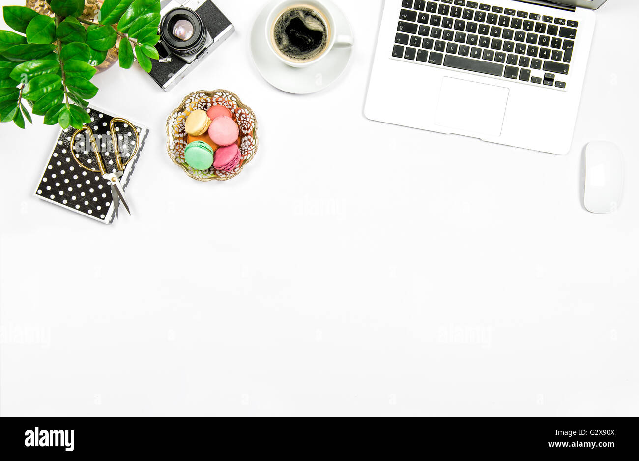 Kreative feminine Arbeitsplatz. Kaffee, Kekse Makronen, Laptop-Computer und Grünpflanze auf weißen Tabellenhintergrund Stockfoto