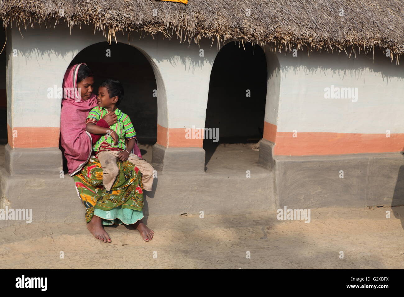 eine Stammes-Dame mit ihrem Sohn in ihrem schönen Lehmhütte in Raiganj, Westbengalen Stockfoto