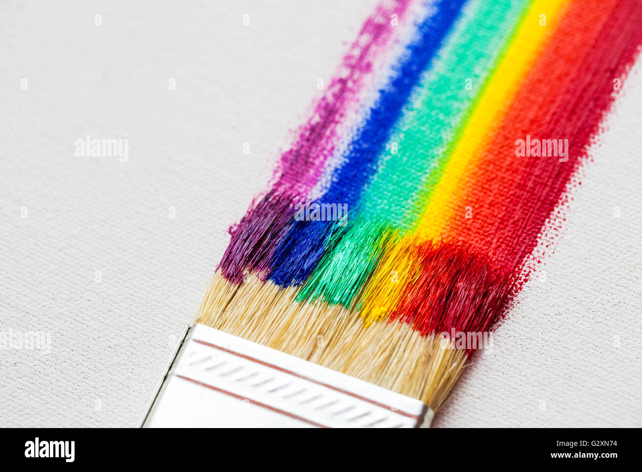 Flacher Pinsel und mehrfarbige Regenbogenpinselstriche auf weißer Künstlerleinwand Stockfoto