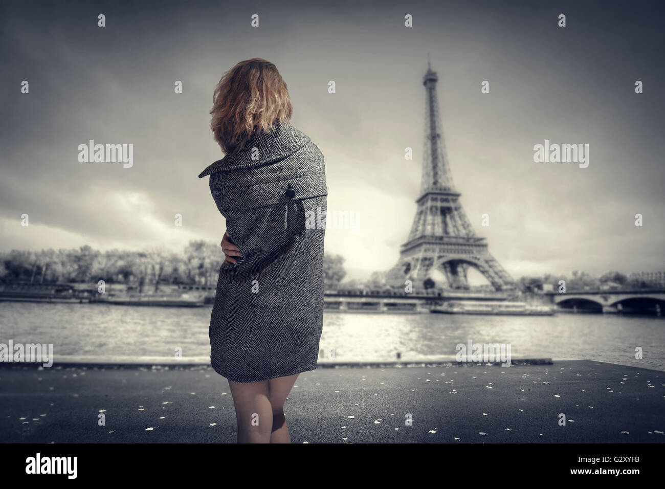 Frau im Mantel stehen an den Ufern der Seine, Blick auf den Eiffelturm. Stockfoto