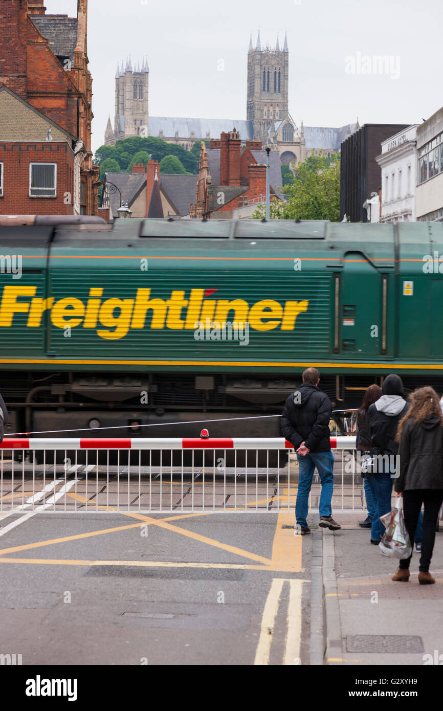 Menschen / Fußgänger warten auf eine Eisenbahn Bahnübergang Barriere in Lincoln, Lincolnshire, UK, während ein Güterzug durchläuft. Stockfoto