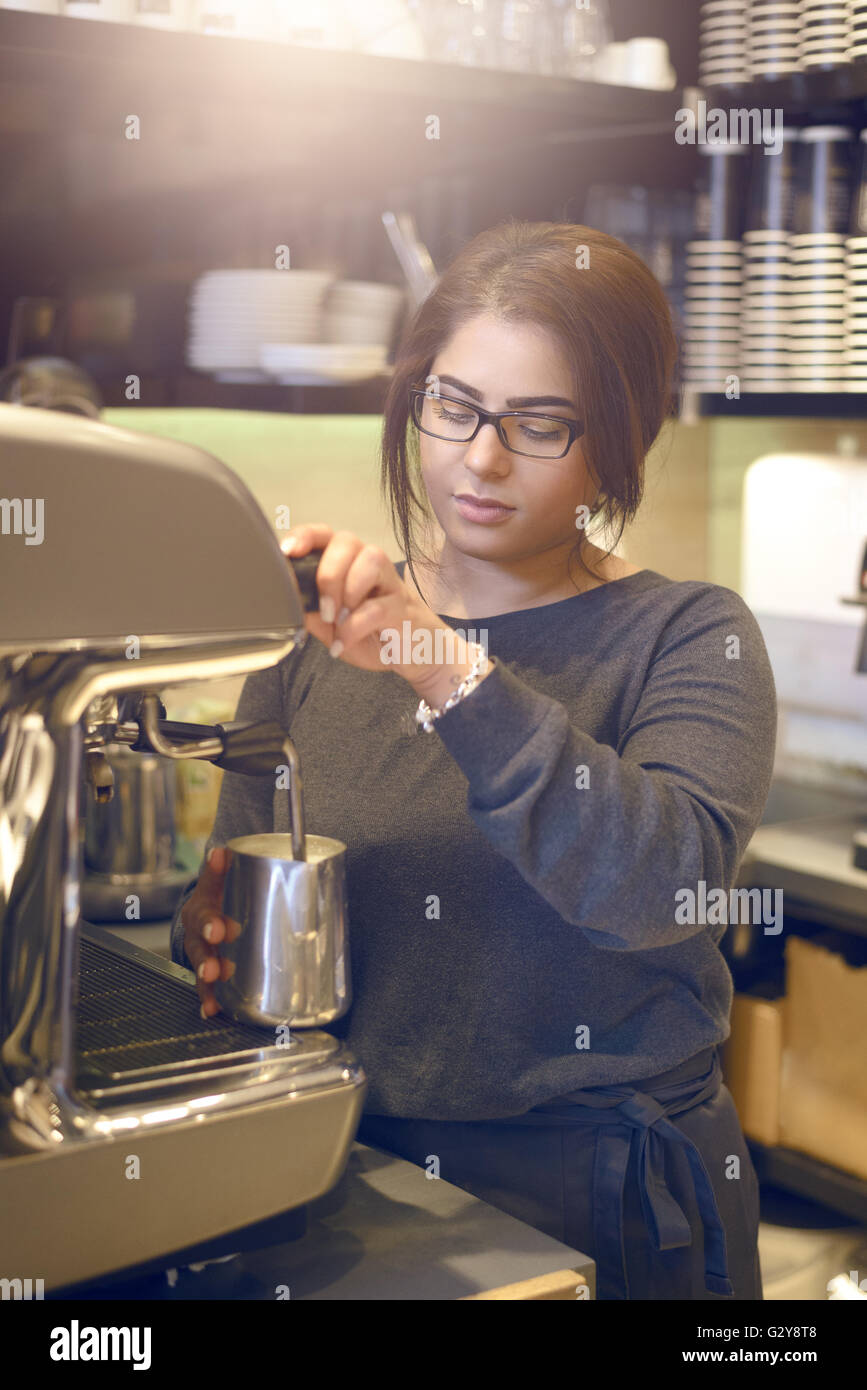 Weibliche Barista oder Kellnerin mache eine Tasse Cappuccino in einem Kaffeehaus oder in der Cafeteria der heiße aufgeschäumte Milch in den Kaffee gießen Stockfoto