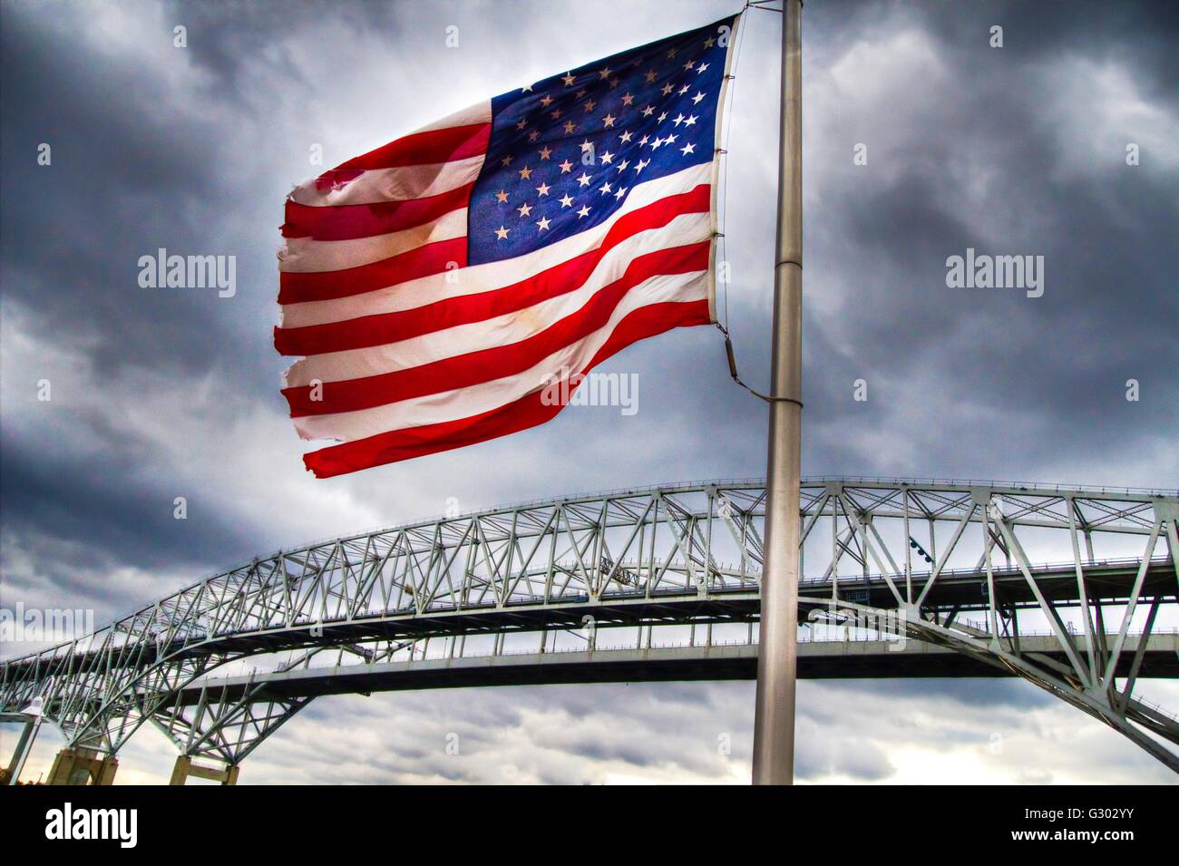 Amerikanische Flagge. Amerikanische Flagge mit der Blue Water Bridge internationalen Grenzübergang als Kulisse. Dies ist die Grenze. Stockfoto