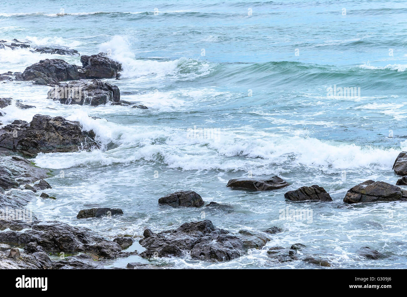 Wellen brechen sich am felsigen Küste. Spritzer auf einem Hintergrund von Steinen. Stockfoto