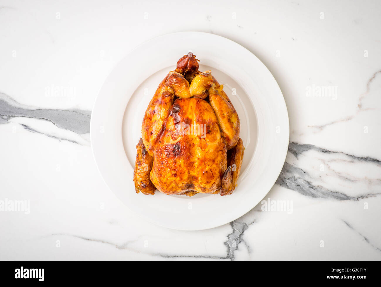 Brathähnchen. Ganze Brathähnchen auf weißen Teller auf Marmor Arbeitsfläche von oben gesehen Stockfoto
