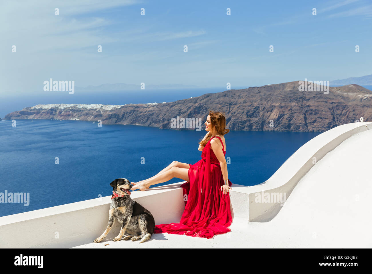 Frau im roten Kleid am Rande des Daches, Blick auf das Meer, in der Nähe ein schöner Hund Stockfoto