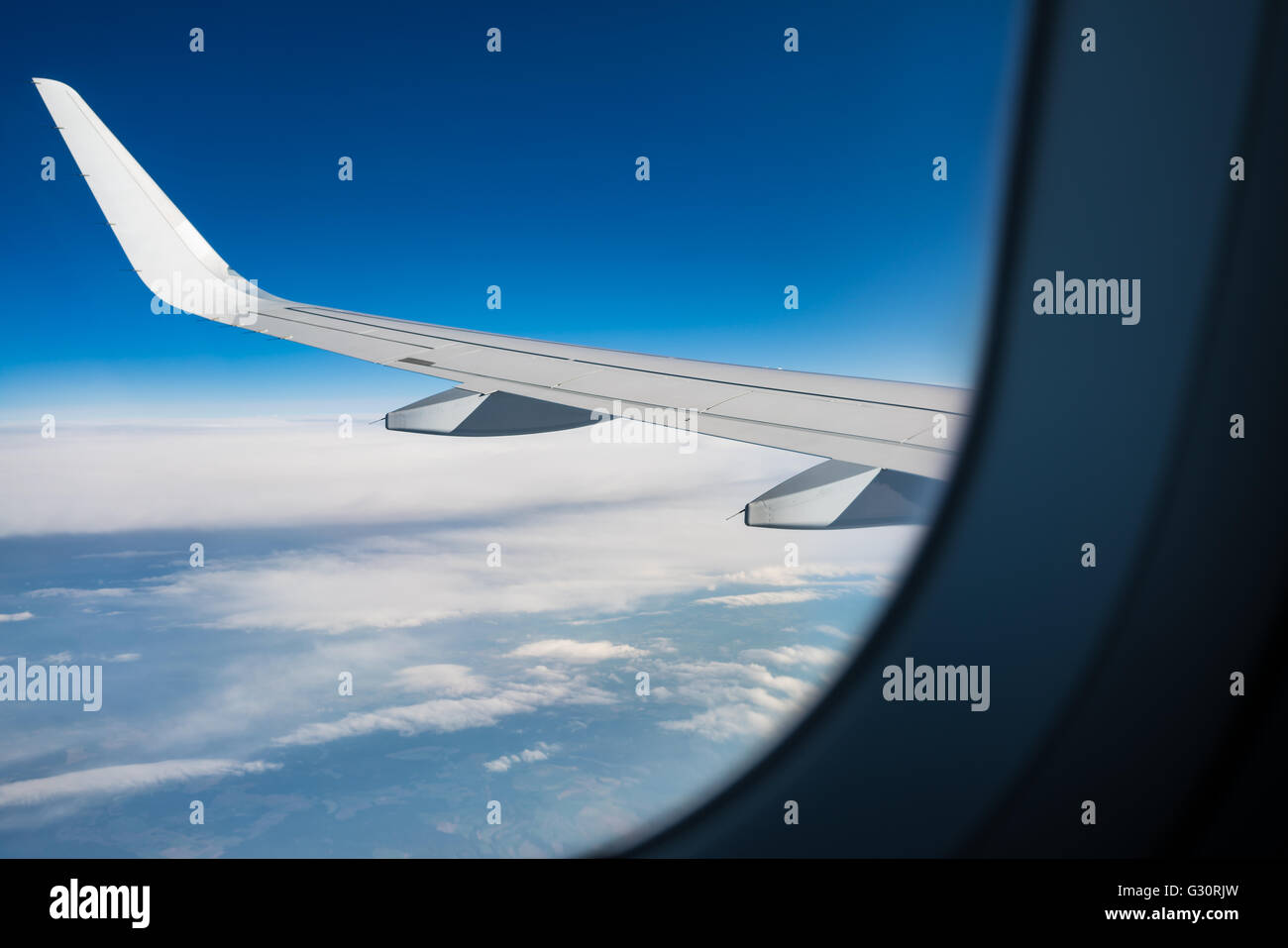 BLICK DURCH EIN FENSTER EIN PASSAGIERFLUGZEUG MIT DEM FLÜGEL IM BLICK UND EINEN BLAUEN WOLKENHIMMEL MIT LAND BALG Stockfoto