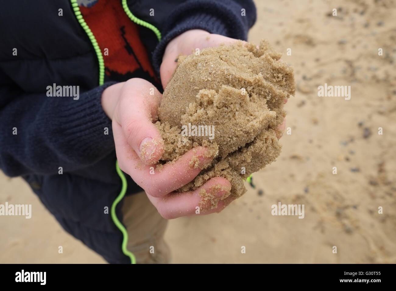 Des Kindes Hände halten einen Haufen Sand am Strand Stockfoto