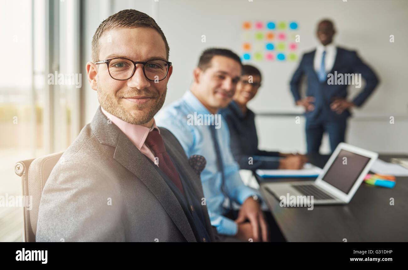 Gut aussehend bärtiger Mann mit Anzug und Krawatte, mit drei professionelle Mitarbeiter in Sitzung am Konferenztisch vor eine große Stockfoto