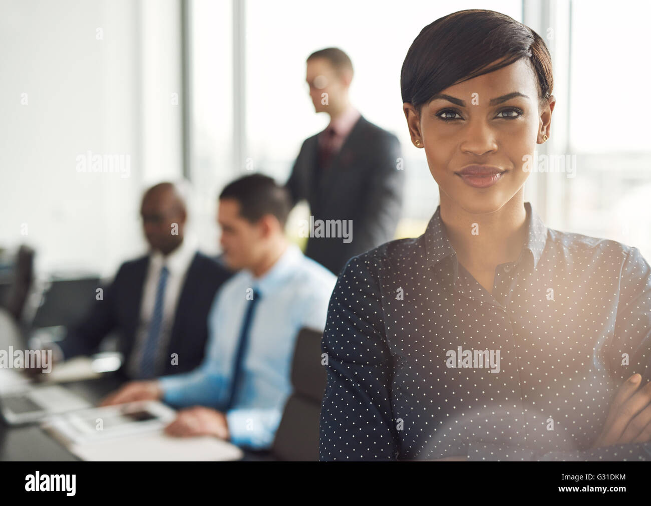 Attraktive junge grinsenden Unternehmer im Büro mit Polka Dot Bluse, verschränkten Armen und zuversichtlich Ausdruck vor Gruppe Stockfoto