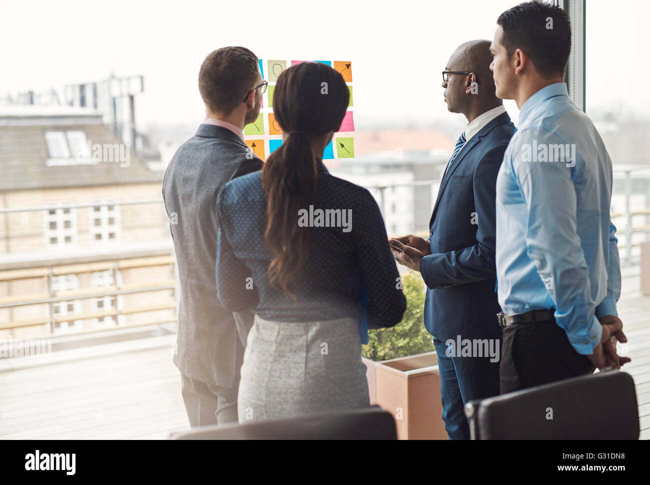 Vier verschiedene Rassen Geschäftsleute stehen in einer Gruppe vor einem hohen zentralen Fenster Blick auf eine Reihe von bunten Memos stu Stockfoto