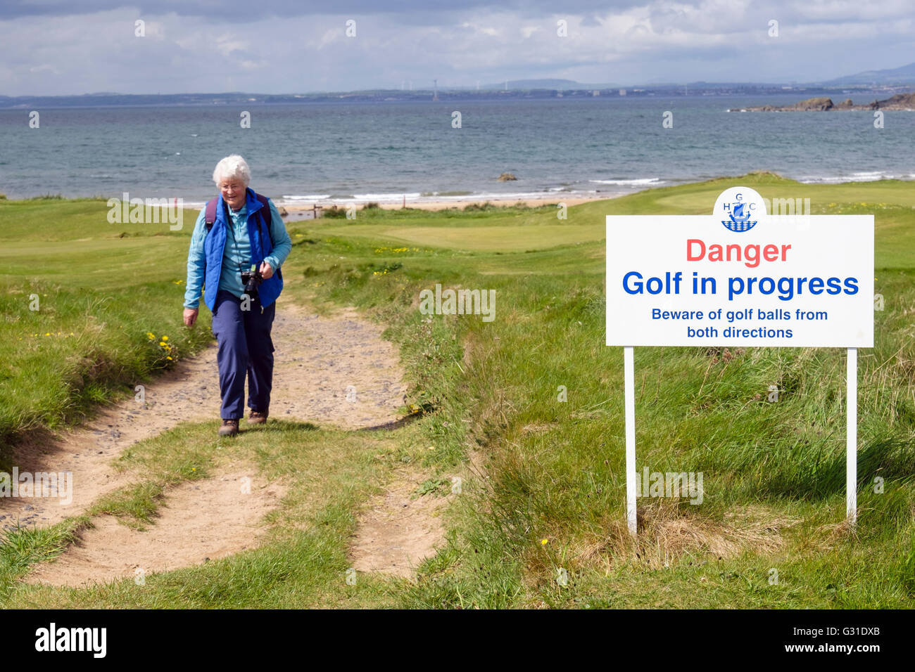Ältere Frau zu Fuß auf Fife Coastal Path mit Warnschild vom Earlsferry Links-Golfplatz. Elie und Earlsferry Fife Schottland UK Stockfoto