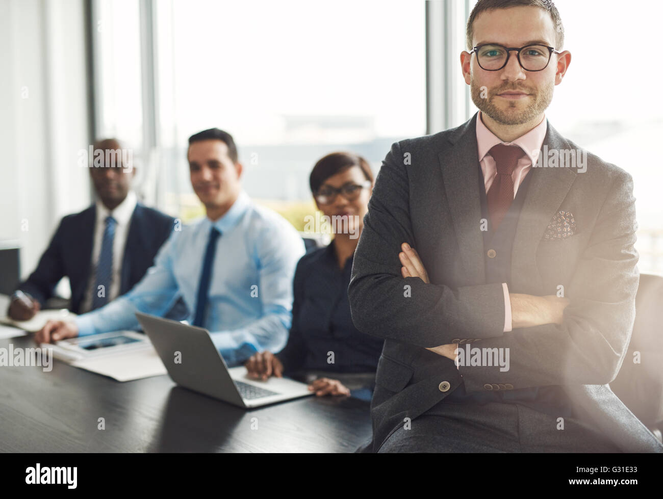 Gut aussehend bärtigen Profi sitzen am Schreibtisch-Ecke neben drei Mitarbeiter vor große Bürofenster Stockfoto