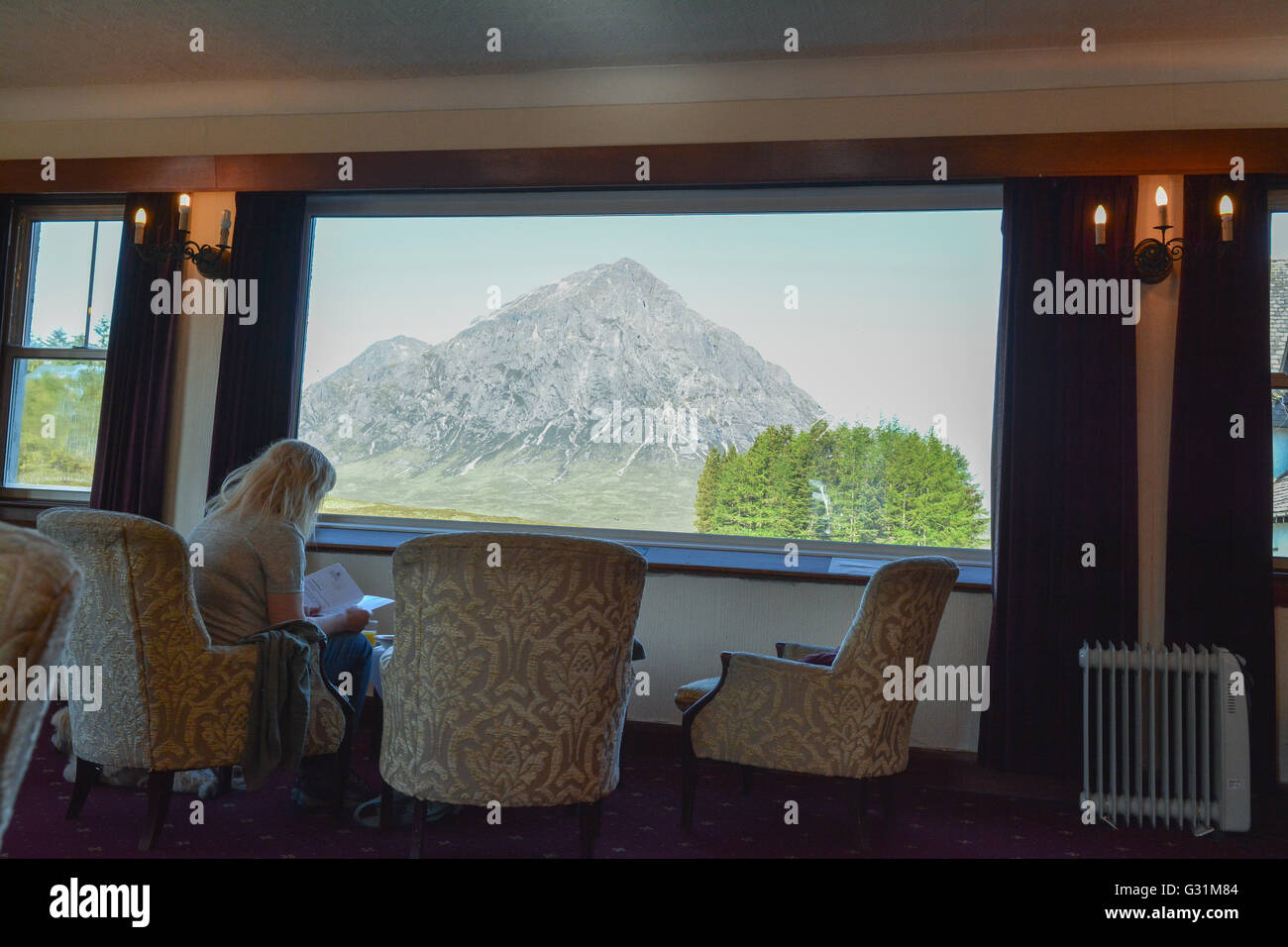 Frau sitzt vor einem atemberaubenden Blick auf Buchaille Etive Mor aus dem Fenster des Kings House Hotel, Glencoe, Schottland, Vereinigtes Königreich Stockfoto