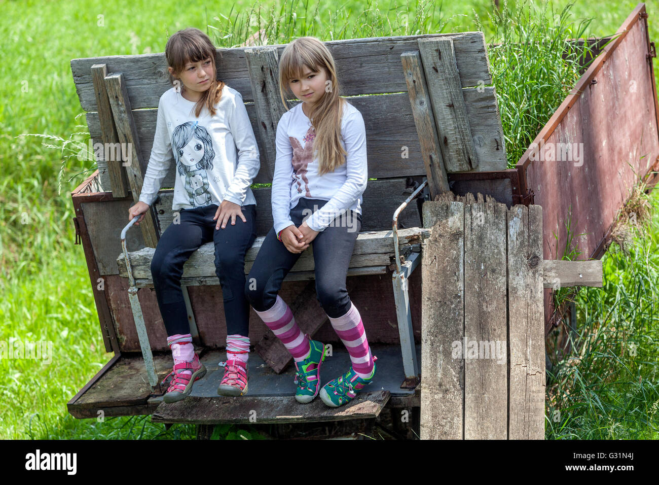 Zwei Mädchen, die sechs sieben Jahre alt sind, in einem Sommerkleid, sitzen auf einem alten Pritschenbett Stockfoto
