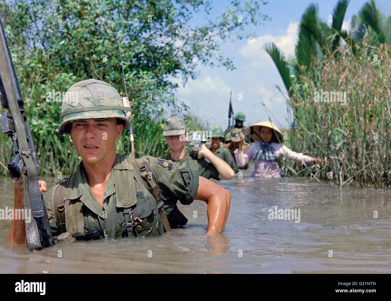 US-Armee Soldaten PFC Fred Greenleaf, mit C Company, 3. Bataillon, 7. Infanterie-Division, 199. Light Infantry Brigade, überquert eine tiefe Bewässerungskanal zusammen mit Mitgliedern der 5. ARVN Ranger Gruppe auf dem Weg zu einem Vietcong kontrollierten Dorf während des Betriebs klingelte Dong 21. November 1967 in Cat Lai, Südvietnam. Stockfoto