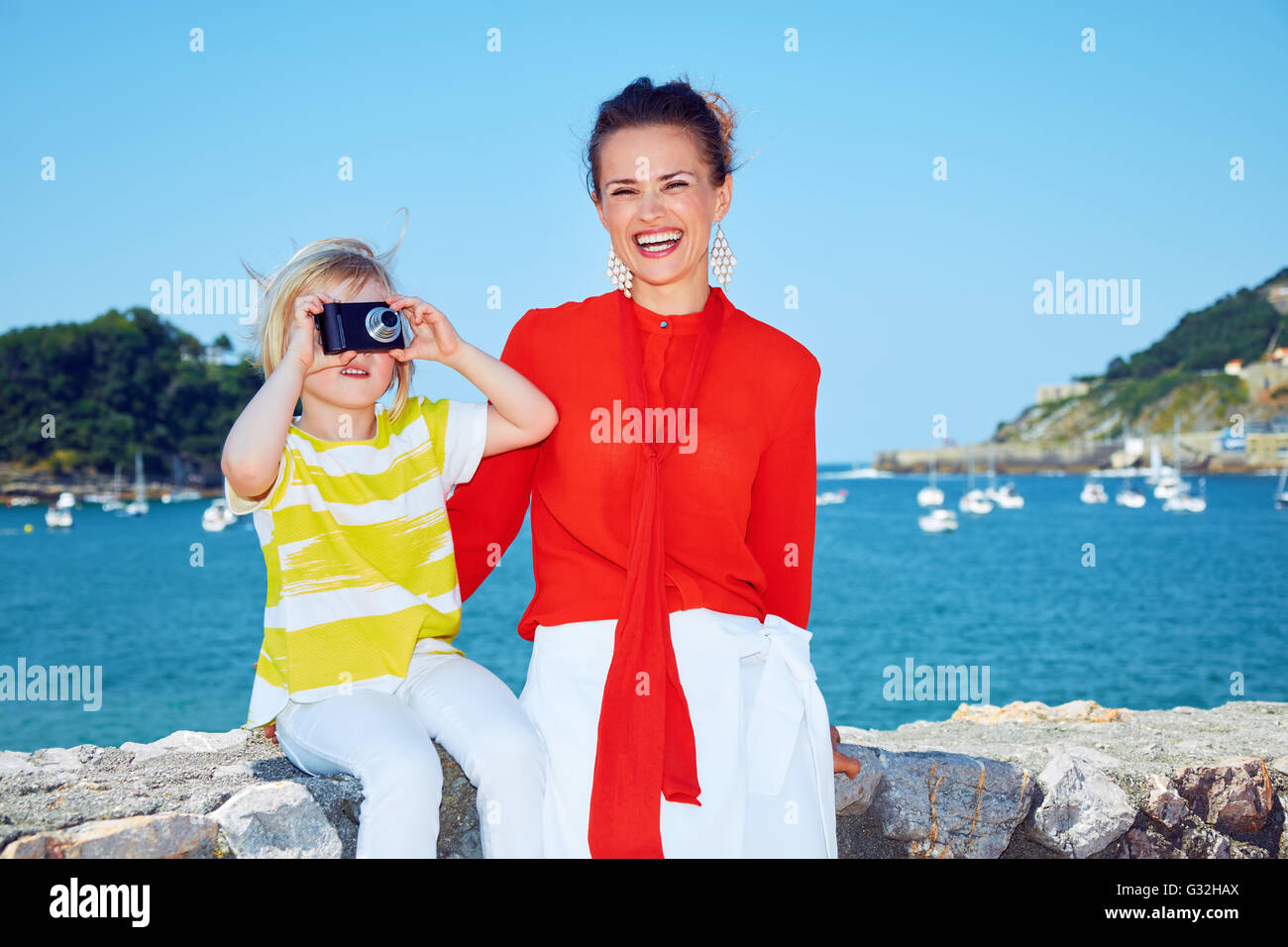 Luxus Wochenende mit der Familie. Glückliche Mutter und Kind nehmen Foto mit Digitalkamera vor der wunderschönen Kulisse mit Blick auf Lagune mit Yachten Stockfoto