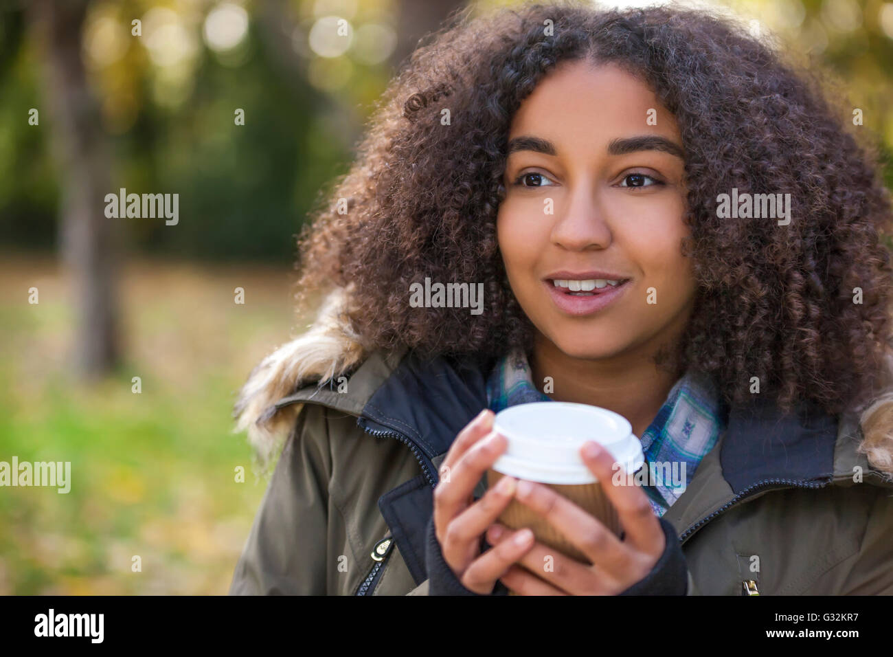 Schöne glückliche Mischlinge afroamerikanische Mädchen Teenager weibliche junge Frau lächelt, trinken Kaffee zum Mitnehmen außerhalb Stockfoto