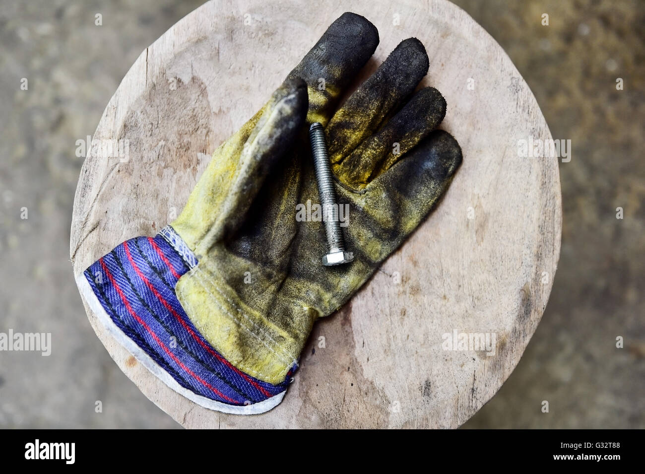 Schmutzige Arbeitnehmers Handschuh mit einer Schraube auf ein Holzbrett in eine Werkstatt Stockfoto