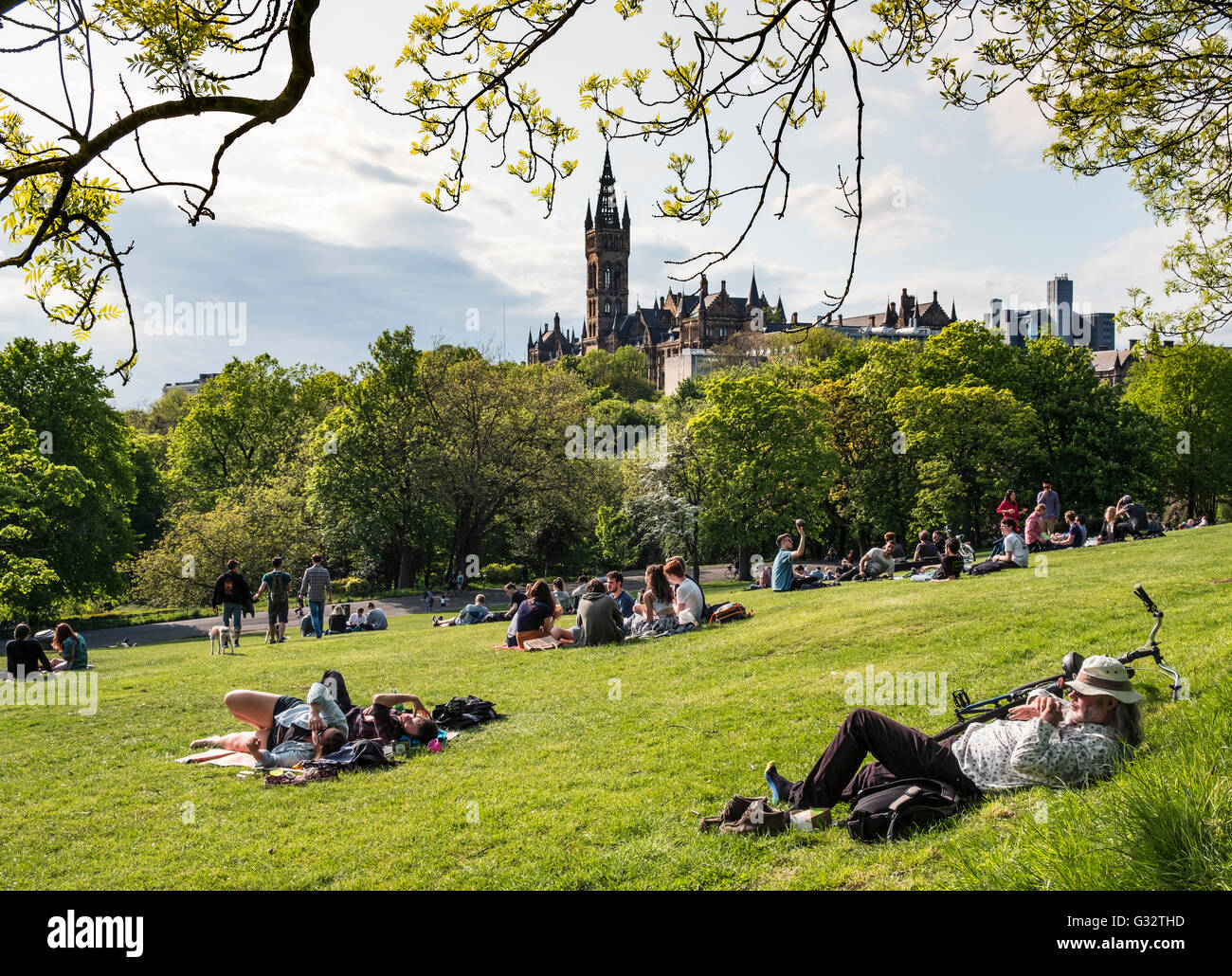 Studenten, die entspannend auf Rasen von Kelvingrove Park mit der Glasgow University in der Ferne in Schottland, Vereinigtes Königreich Stockfoto