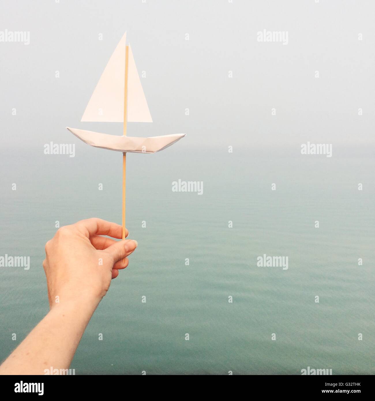 Zarte Frauenhand hält ein Papierschiff vom Ozean Stockfoto