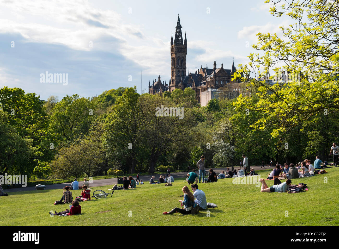 Studenten, die entspannend auf Rasen von Kelvingrove Park mit der Glasgow University in der Ferne in Schottland, Vereinigtes Königreich Stockfoto