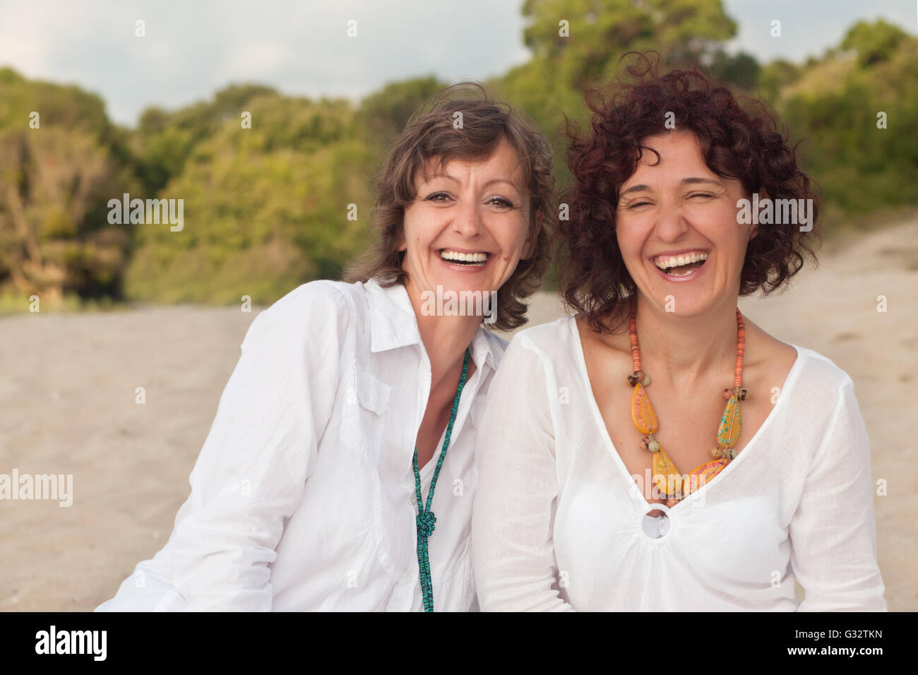 Porträt von zwei lachende Frauen sitzen am Strand Stockfoto