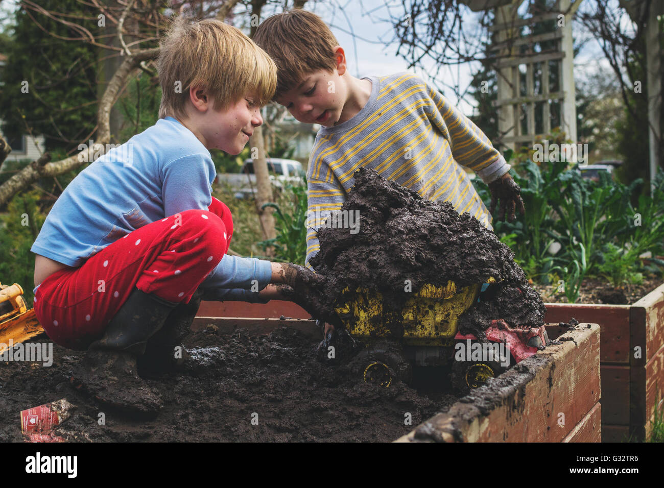 Zwei jungen, die Kunststoff-Spielzeug LKW mit Schlamm im Garten zu füllen Stockfoto
