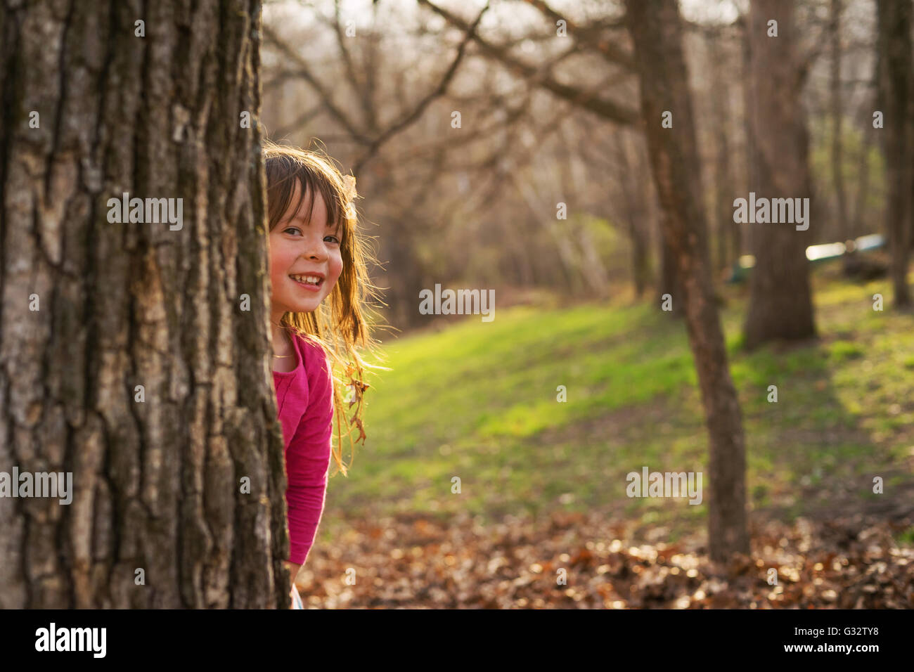 Lächelndes Mädchen versteckt sich hinter einem Baum im park Stockfoto