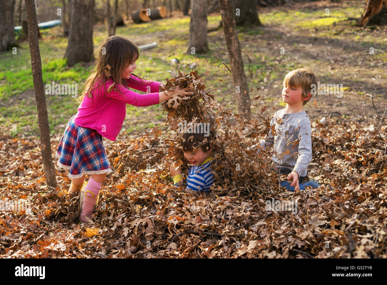 Drei Kinder spielen mit Herbstlaub im park Stockfoto